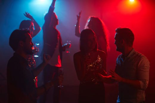 Cheerful friends with flutes talking at party in night club